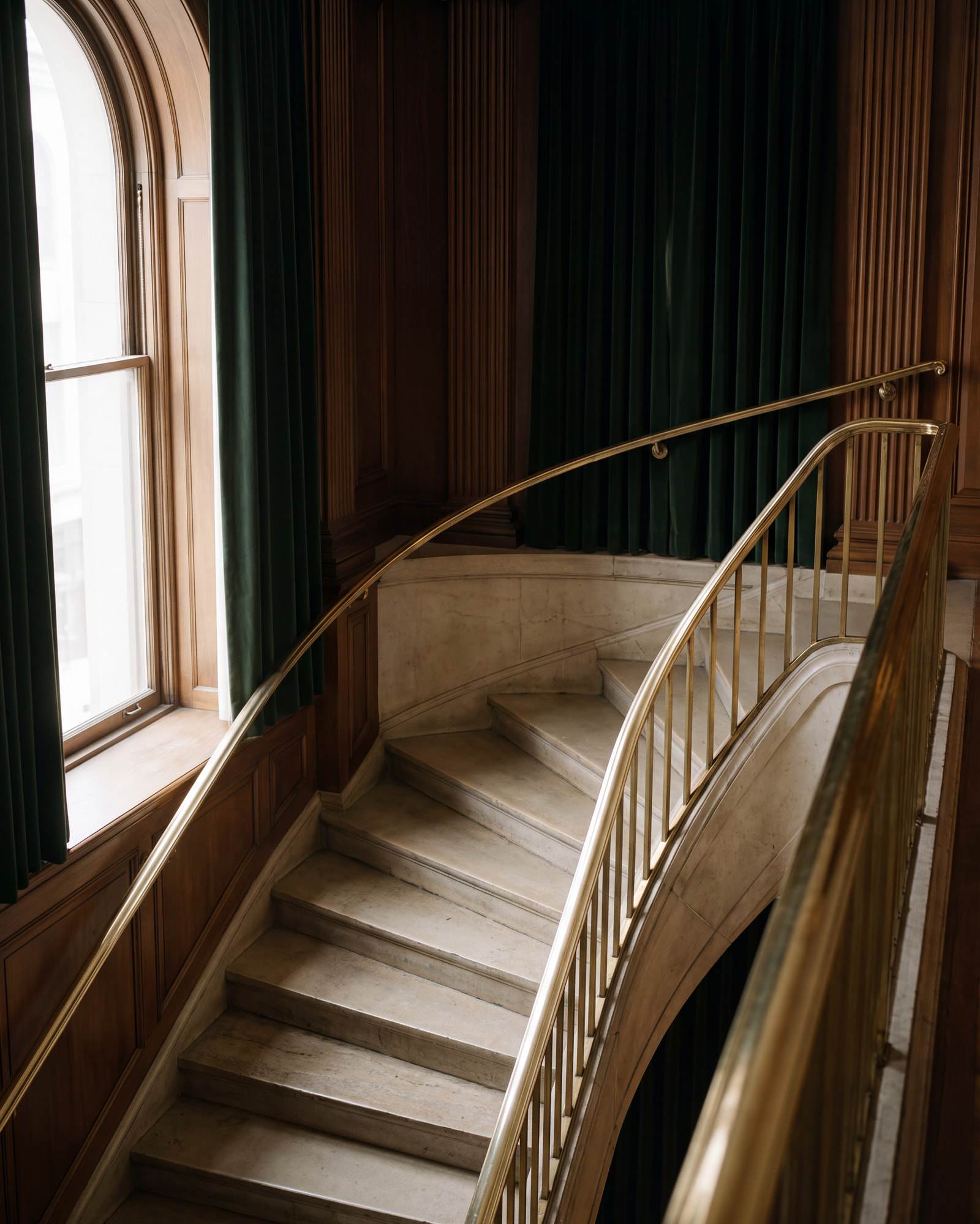 A curving marble staircase with a polished brass handrail and green velvet curtains.